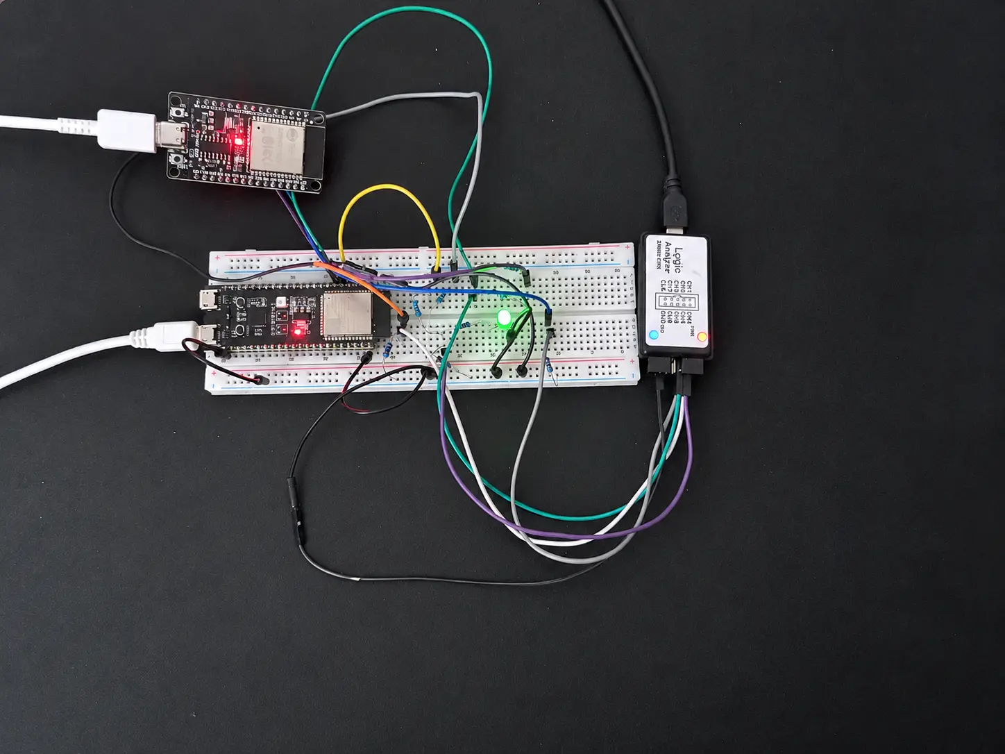 Two ESP32 boards wired on a breadboard to a status LED and a logic analyzer
